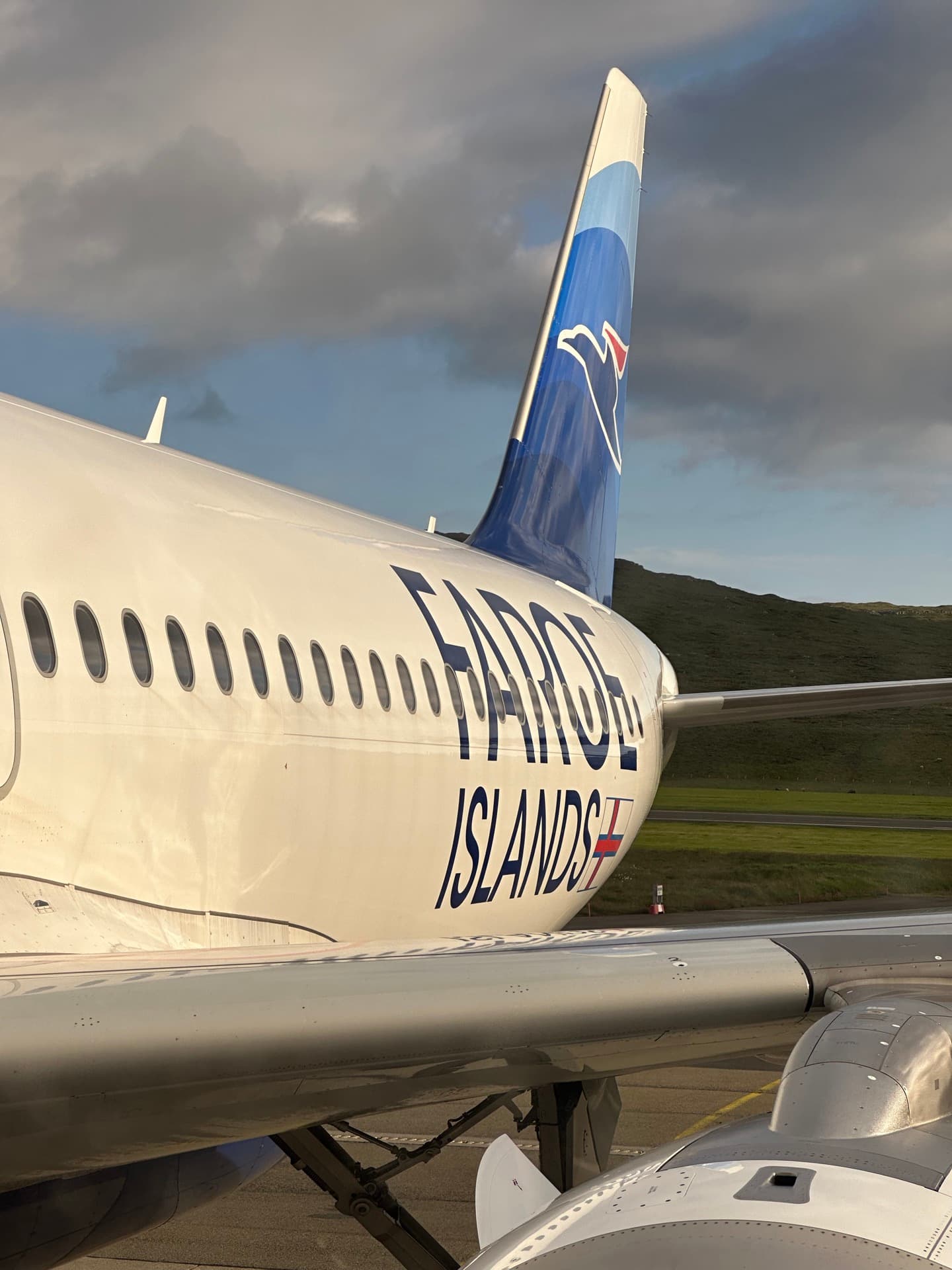 An Atlantic Airways aircraft with Faroe Islands titles parked at Vagar Airport, with green hillside behind