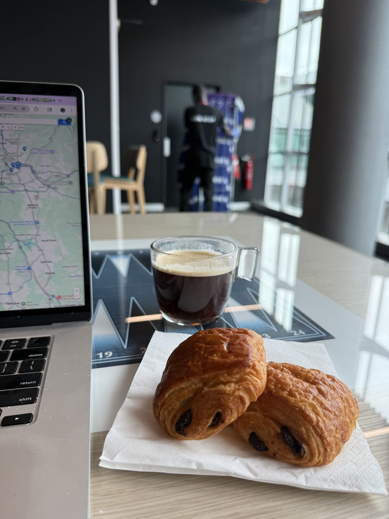 Two pains au chocolat and an espresso on a lounge table beside an open laptop
