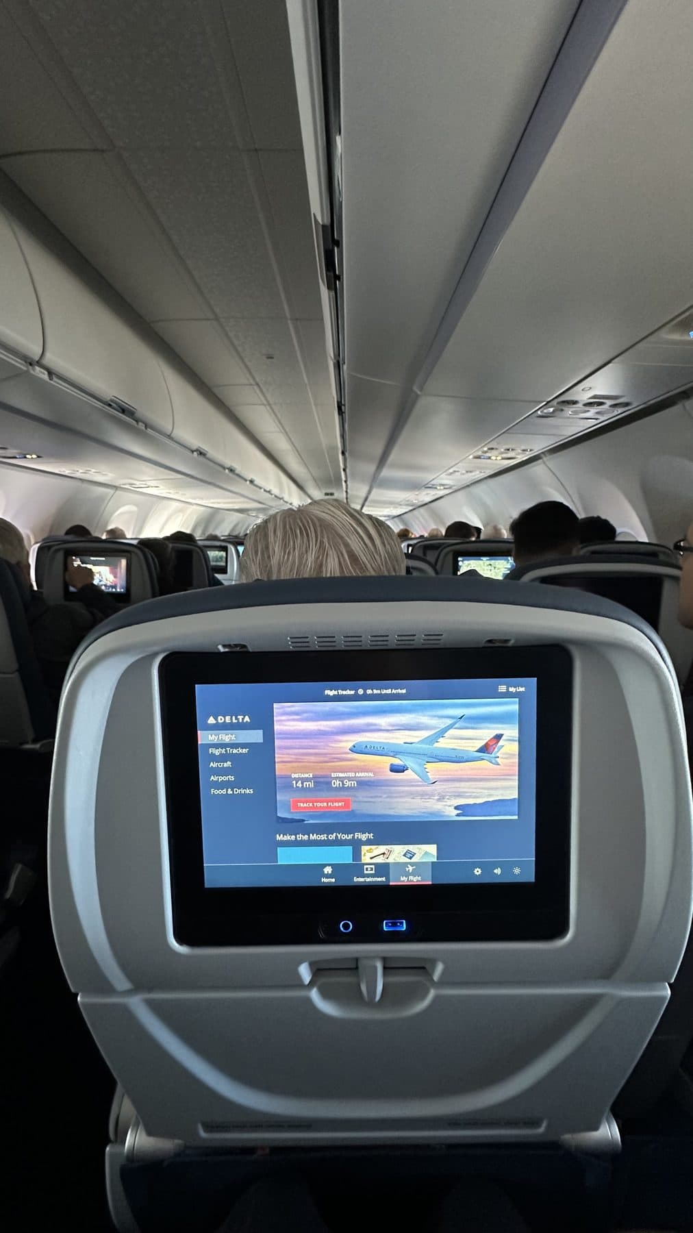 View down a full Delta transatlantic economy cabin, the seatback flight tracker showing nine minutes to arrival in Paris