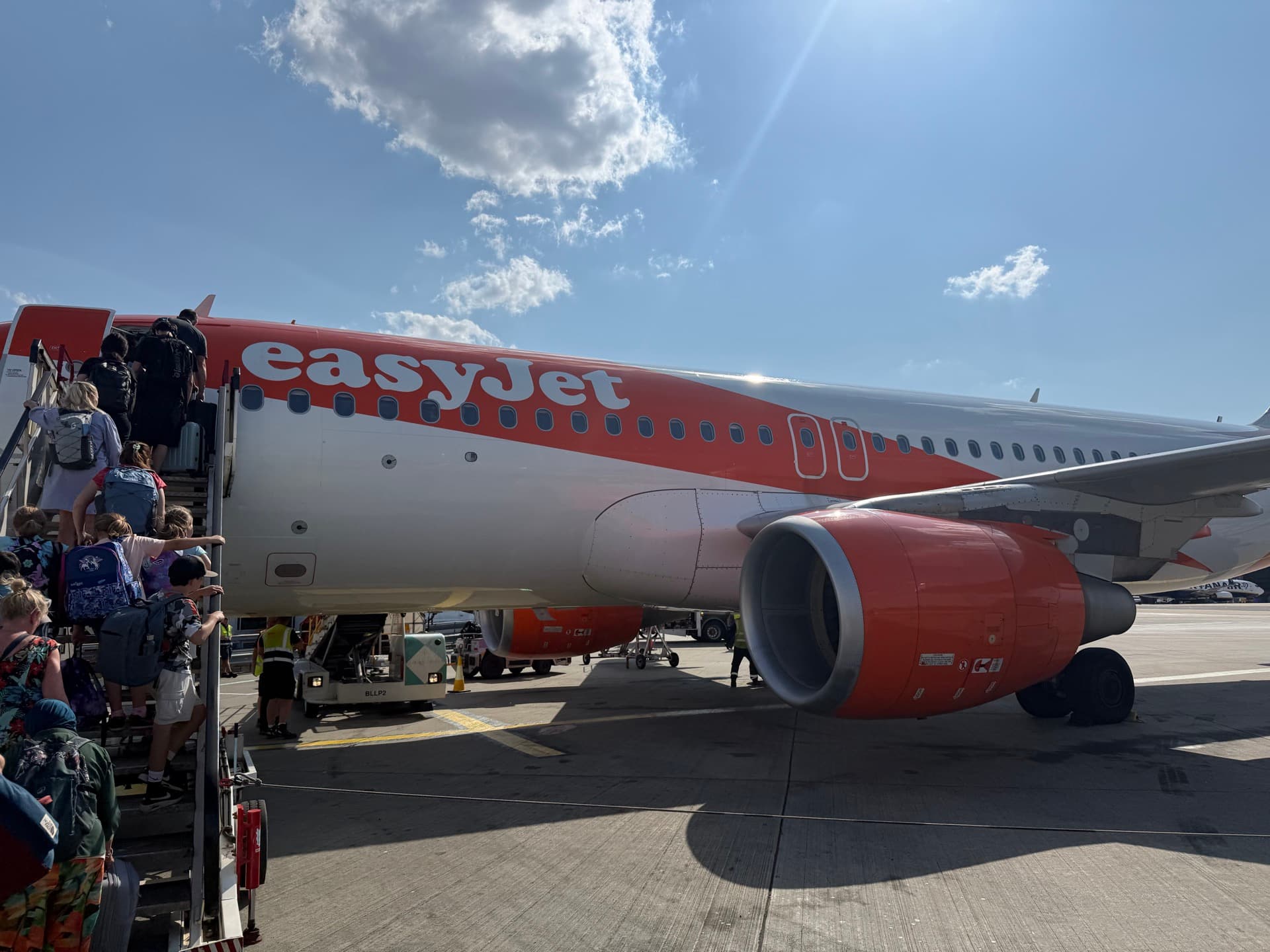 An easyJet Airbus A320 at London Luton with passengers boarding by airstairs from the tarmac