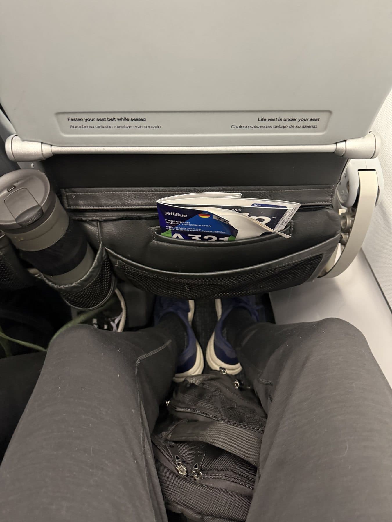 Knee-level view of the legroom in a JetBlue A321 economy seat on a transatlantic flight to London, with a backpack stowed under the seat in front