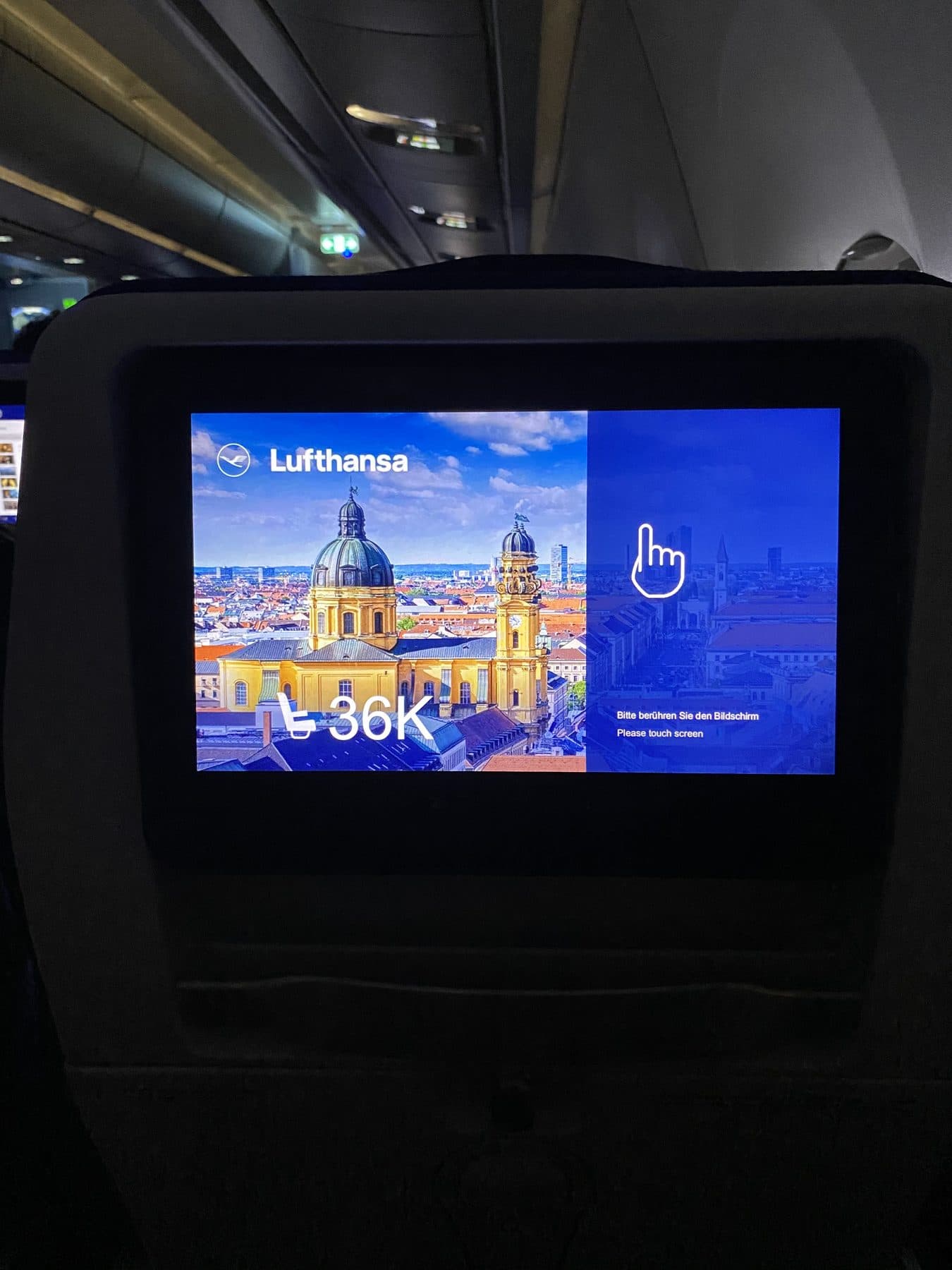 A Lufthansa seatback screen showing seat 36K and a photograph of Munich, on a flight from Boston